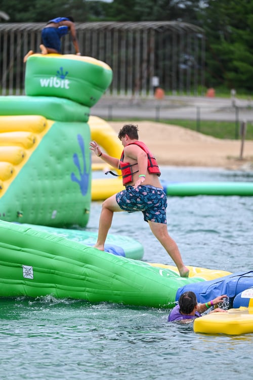 Teenage boy conquers obstacle on Adventure Island, floating water obstacle course, while visiting Bear Paw Adventure Park in the summer. Teenage boy conquers obstacle on Adventure Island, floating water obstacle course, while visiting Bear Paw Adventure Park in the summer.