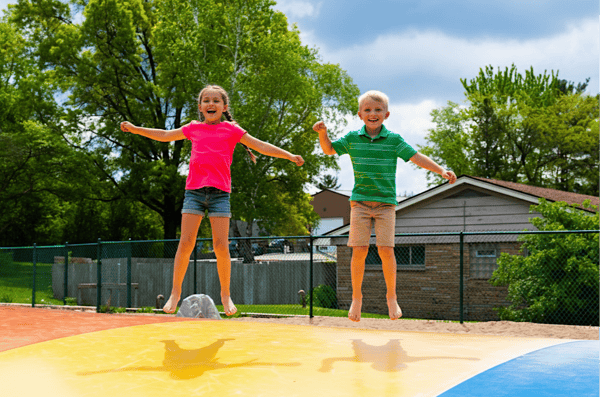 Two young kids bouncing on a jumping pillow on a warm summer day at Jellystone Park™ Caledonia.